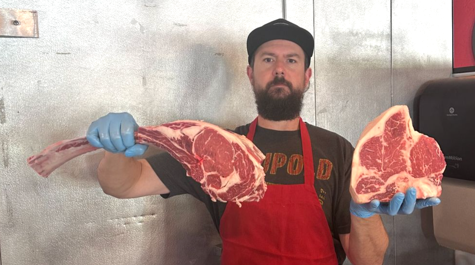 Photo of Nick the butcher holding up a tomahawk chop and porterhouse